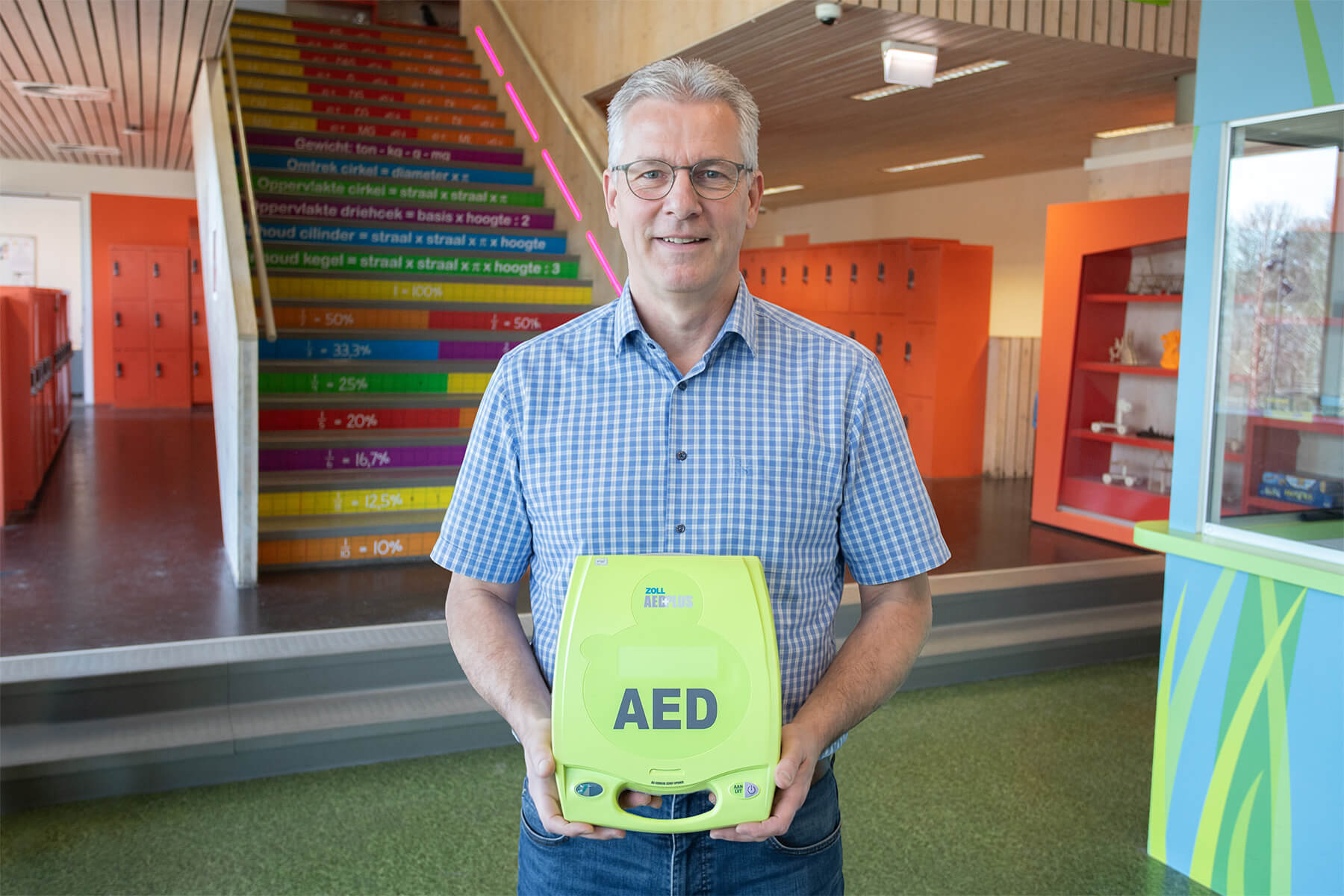 Conciërge van een middelbare school poseert in de hal met een AED